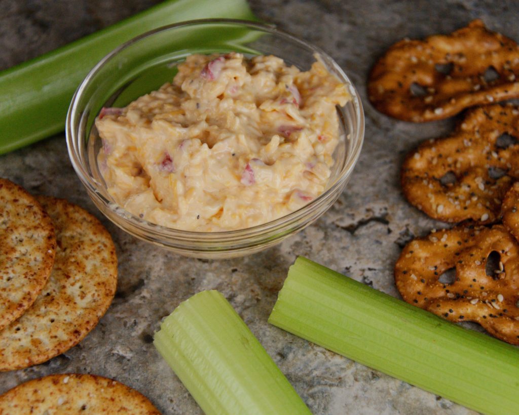 Bowl of pimento cheese with celery, crackers and pretzels. 
