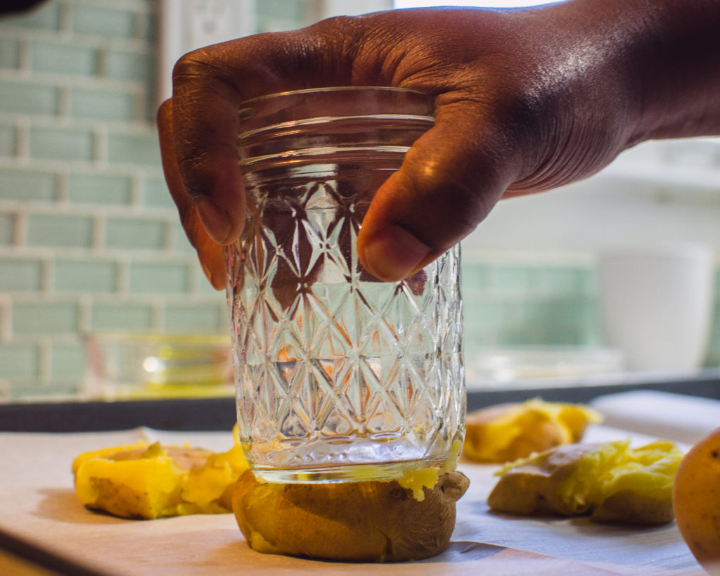 Hand holding a jar that is being pressed down on to a potato to make smashed potatoes.