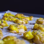 Roasted potatoes topped with herbs and seasoning, ready for serving in a professional kitchen settin.