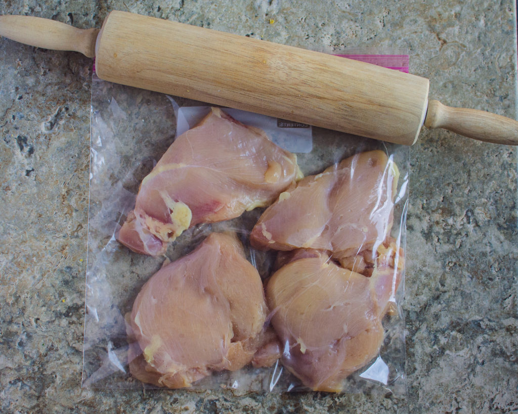 Boneless skinless chicken pieces in a bag with a rolling pin sitting on top. 
