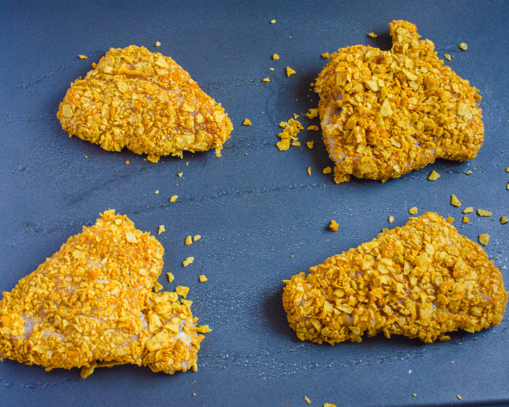 Tortilla crusted chicken prepped on a sheet pan and ready to go in teh oven.