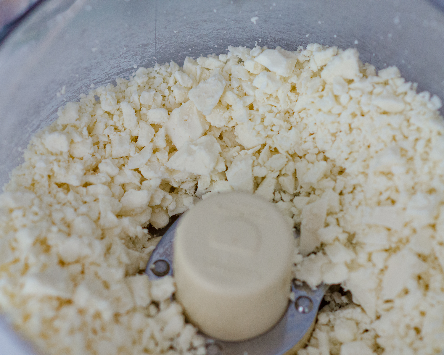 Crumbled feta cheese in the bowl of a food processor. 