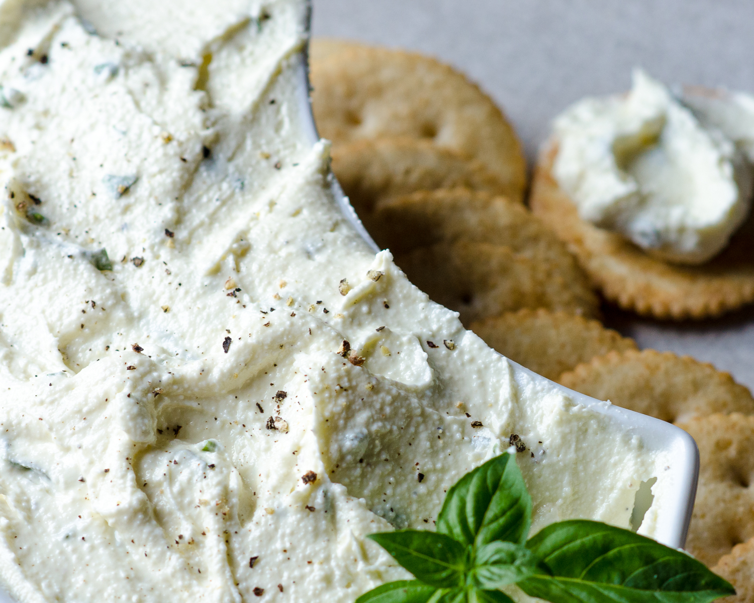 Close up of the whipped feta dip in a serving bowl surrounded by round crackers. Basil on top as garnish. 