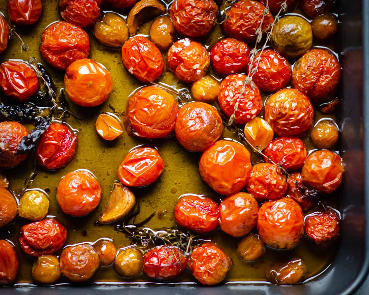 Cooked cherry tomatoes and crispy herbs in a bath of oil in a roastign pan. 