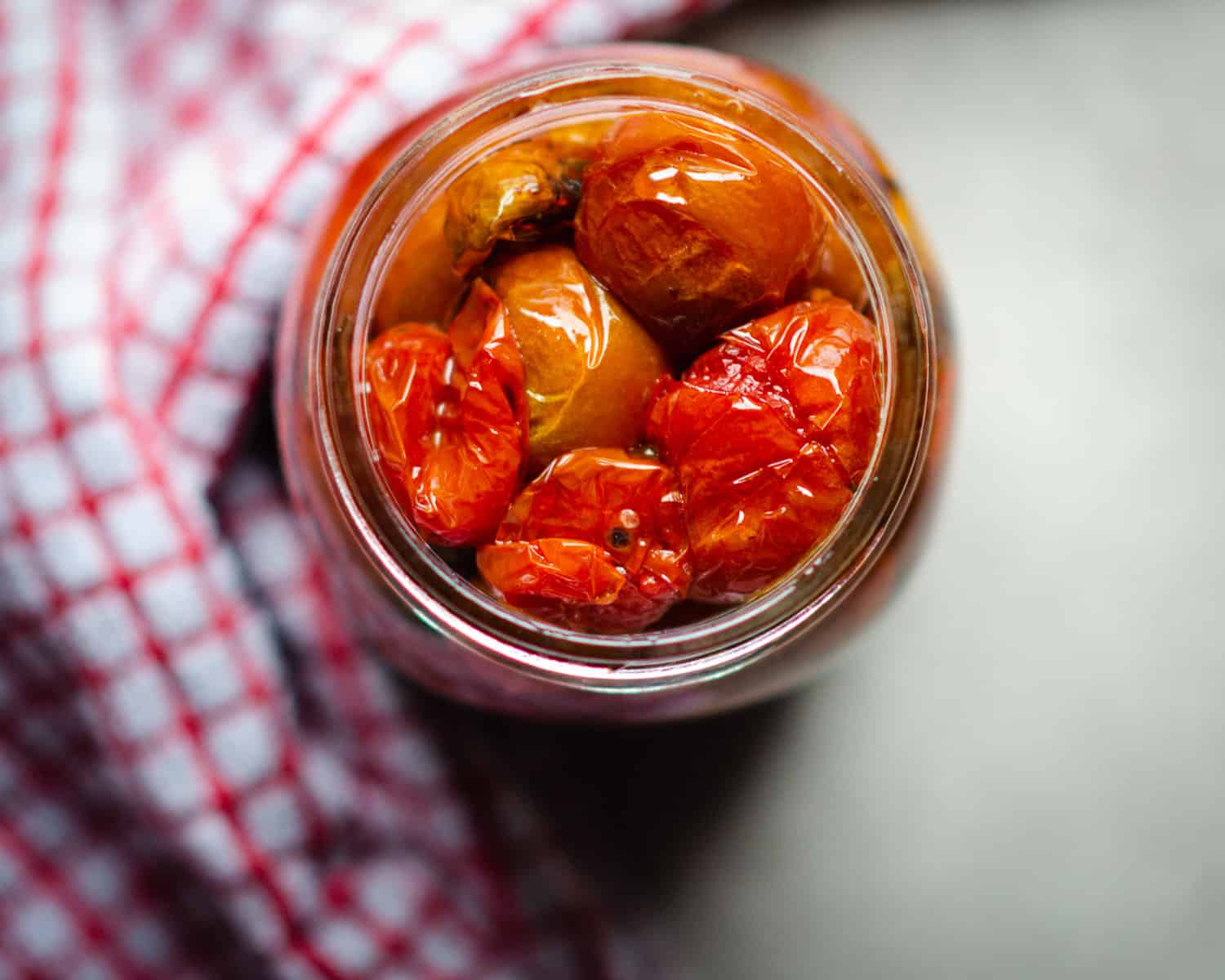 Tomato confit in a mason jar next to a red and white tea towel. 