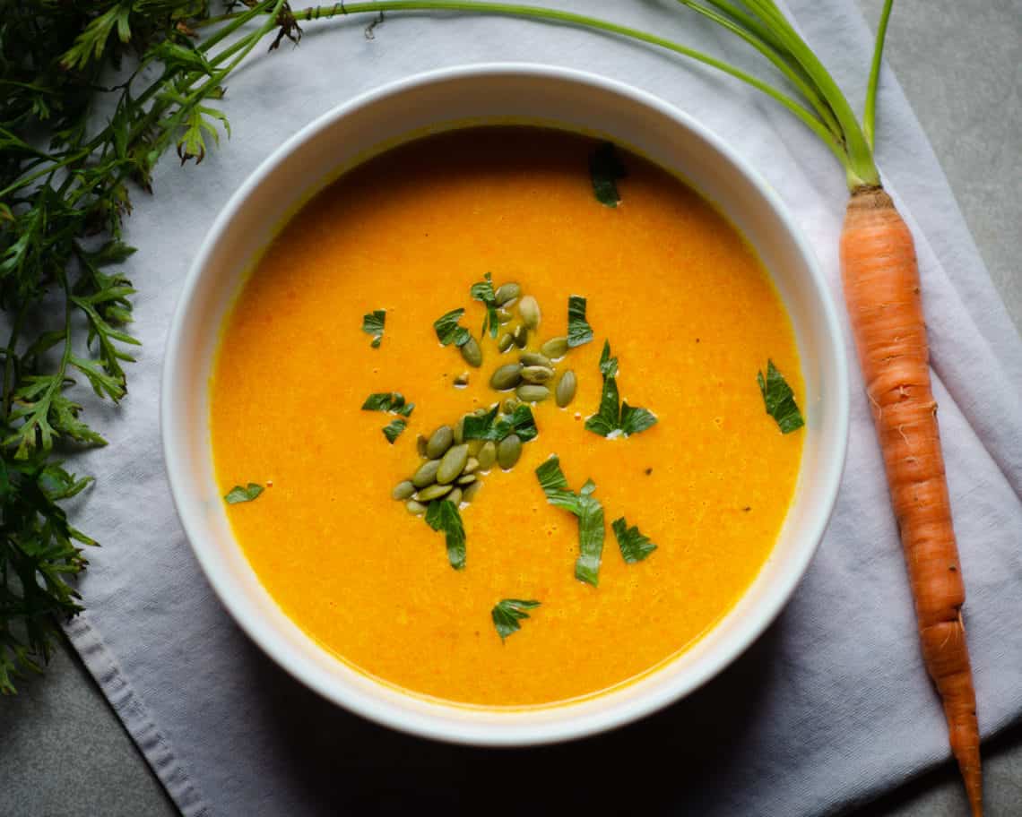 Bowl of carrot and parsnip soup that is garnished with pepitas and parsley