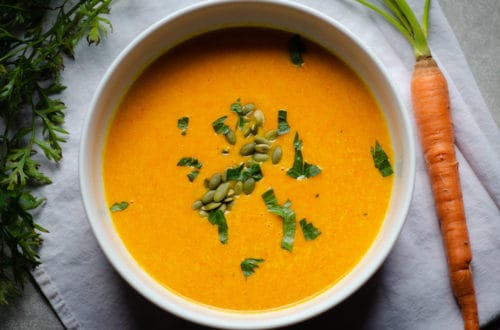 Bowl of carrot and parsnip soup that is garnished with pepitas and parsley