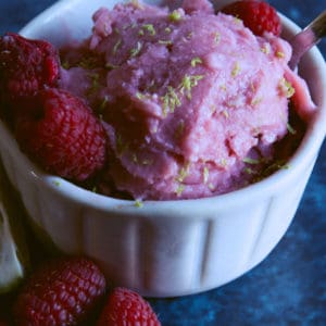 Small bowl of raspberry and lime sherbet with whole raspberries on the side
