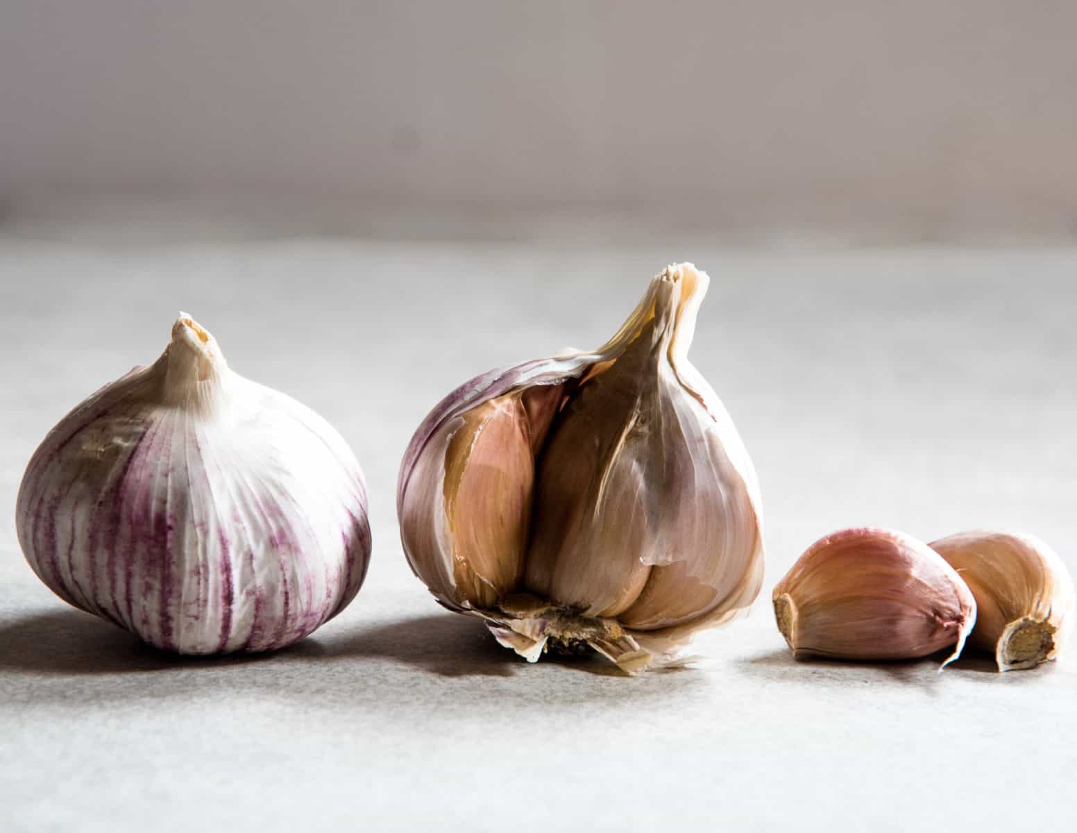 Whole heads of garlic next to two garlic cloves. 