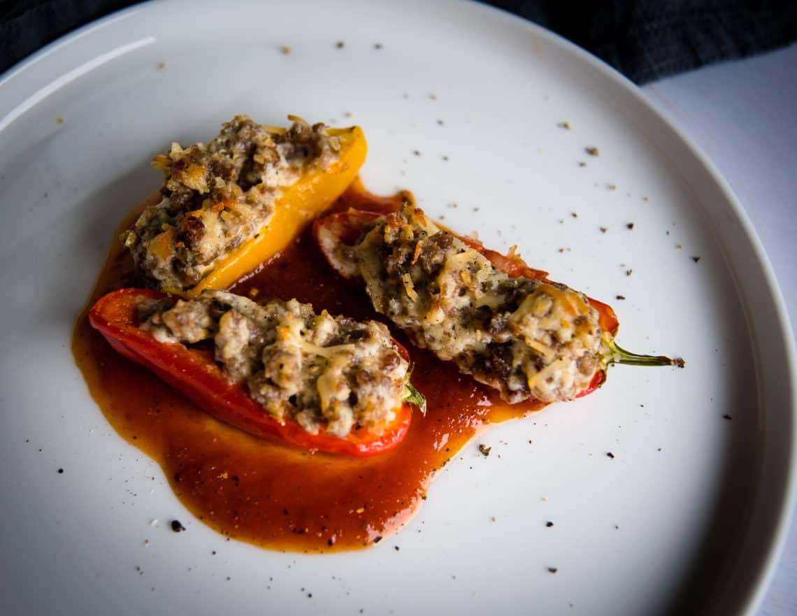 Three stuffed mini bell peppers on top of marinara sauce on a white plate.