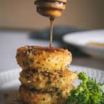Stack of three fried goat cheese slices being drizzled with honey. Parsley sprig on side as garnish.