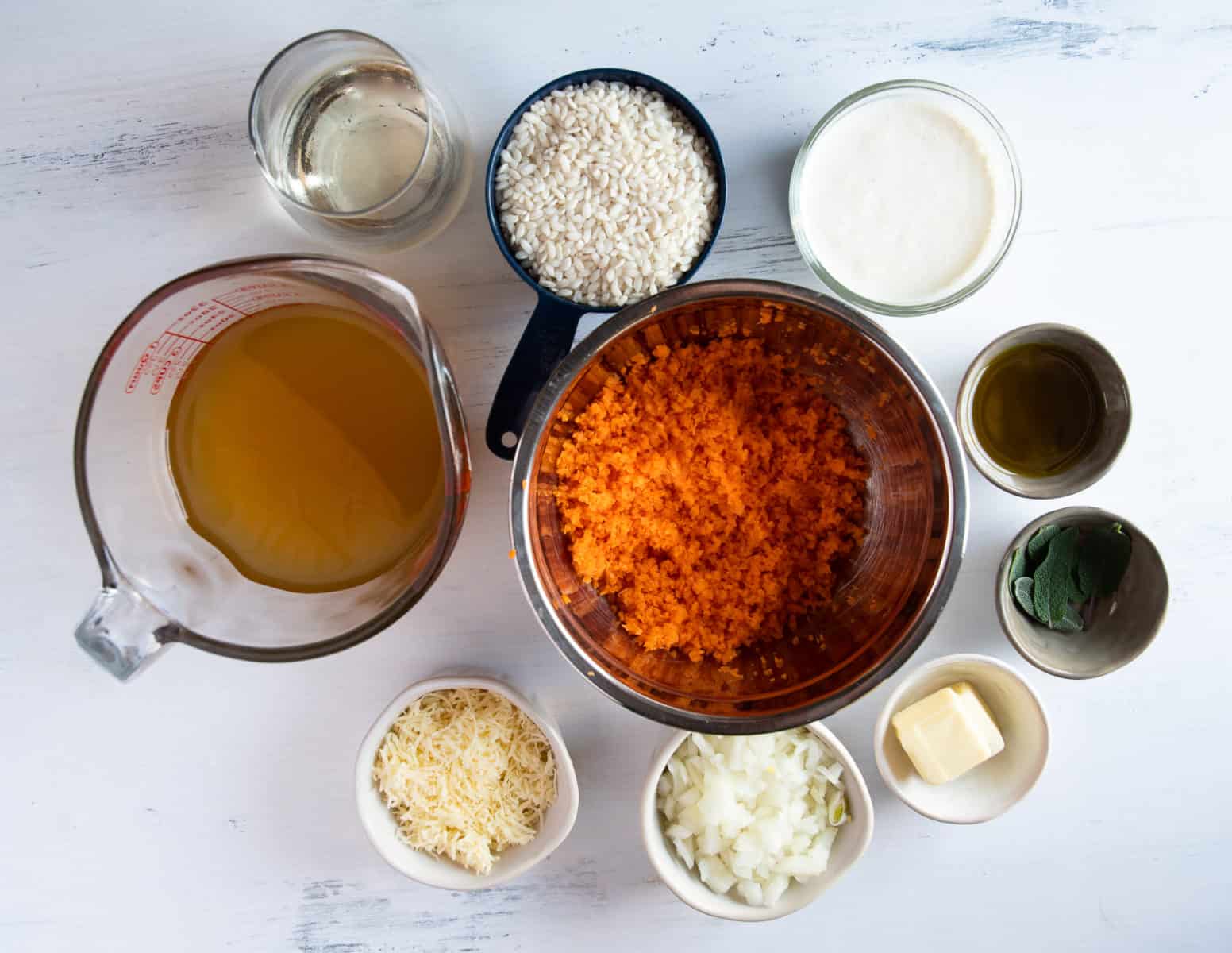 Each ingredient of carrot risotto recipe portioned out into individual bowls and measuring cups. 