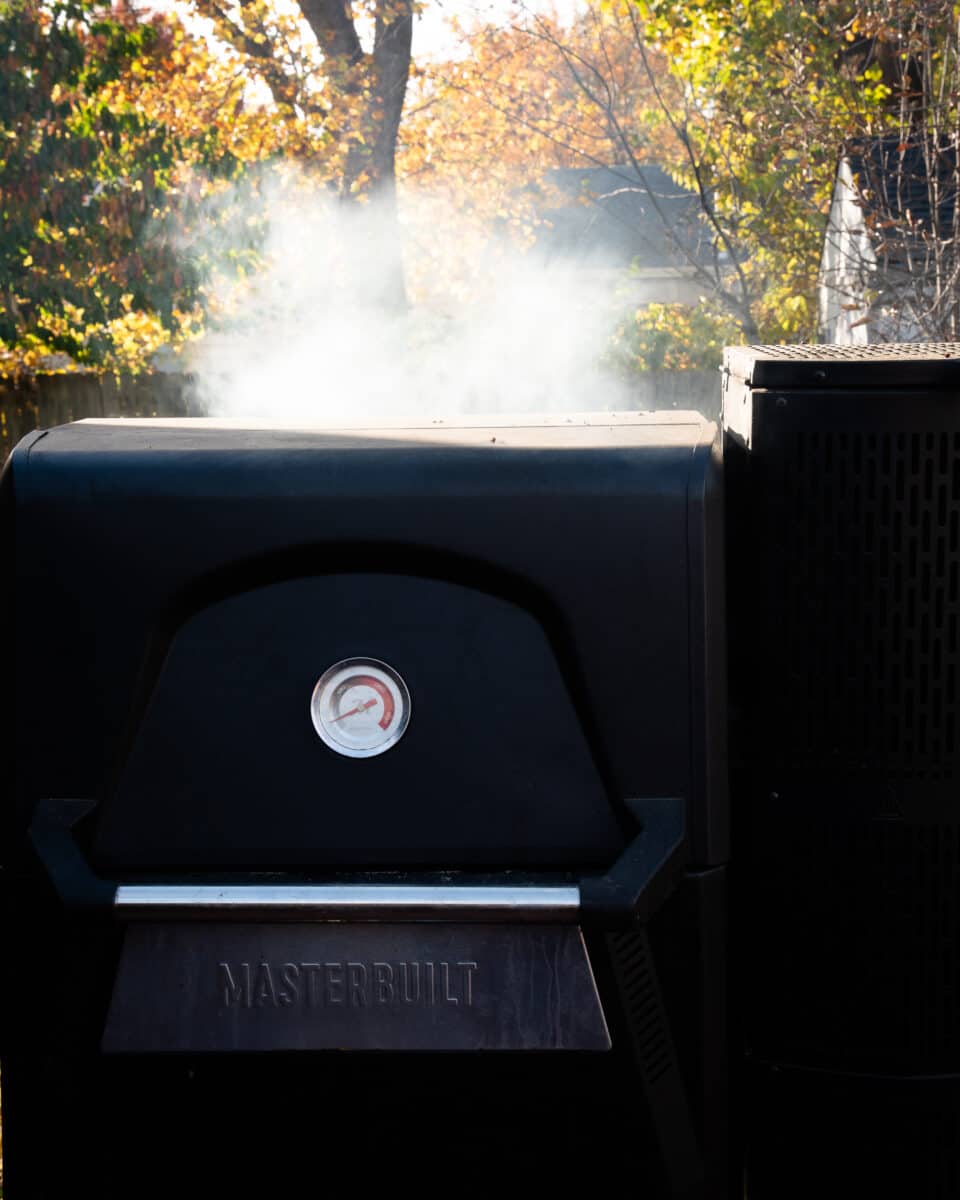 MasterBuilt brand smoker with smoke coming out the top on a deck. 