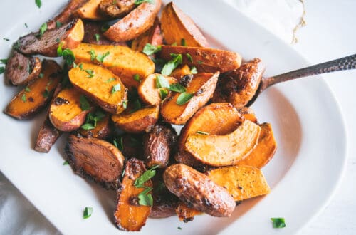Roasted sweet potato fingerling halves on a platter with chopped parsley garnished on top.