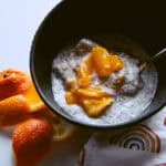 Bowl of sumo orange chia seed pudding with spoon, orange peels on the side and a decorative rainbow napkin.