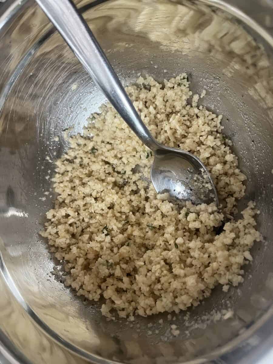 Bowl of breadcrumbs, herbs and oil being stirred with a spoon. 