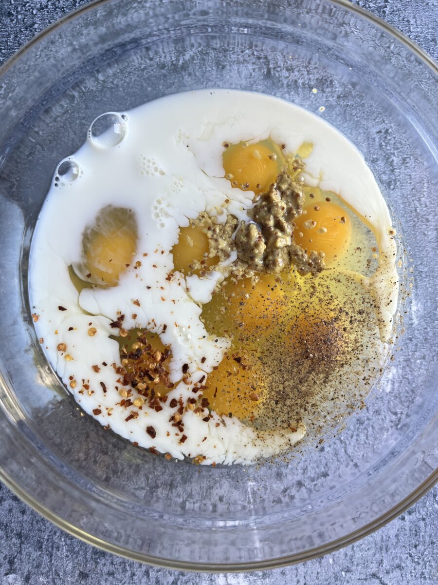 Bowl with unmixed milk, eggs, dijon mustard, and seasonings.
