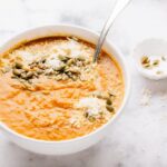 Bowl of apple squash soup with garnish in small bowl on the side.