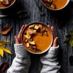 Pumpkin sweet potato soup in three bowls and garnished with croutons, sage, and cooked bacon.